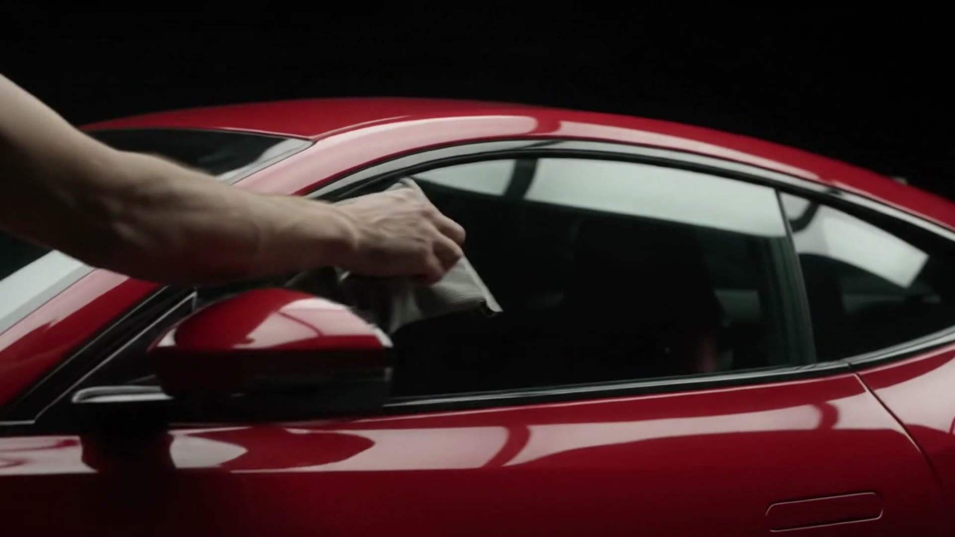 Una mano ripassa con il panno il finestrino di un'auto rossa