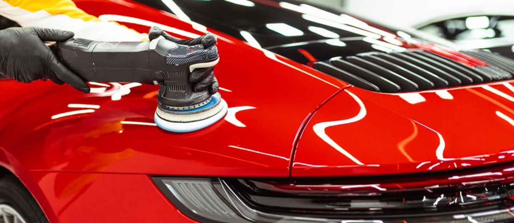 Lucidatrice al lavoro sul cofano di un'auto rossa